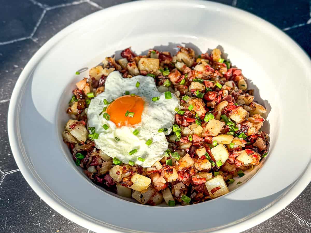 A white bowl containing corned beef hash and a fried egg with chopped chives on top.