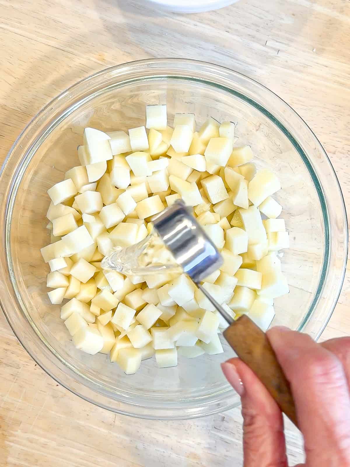 Adding water to diced potatoes in a glass bowl.