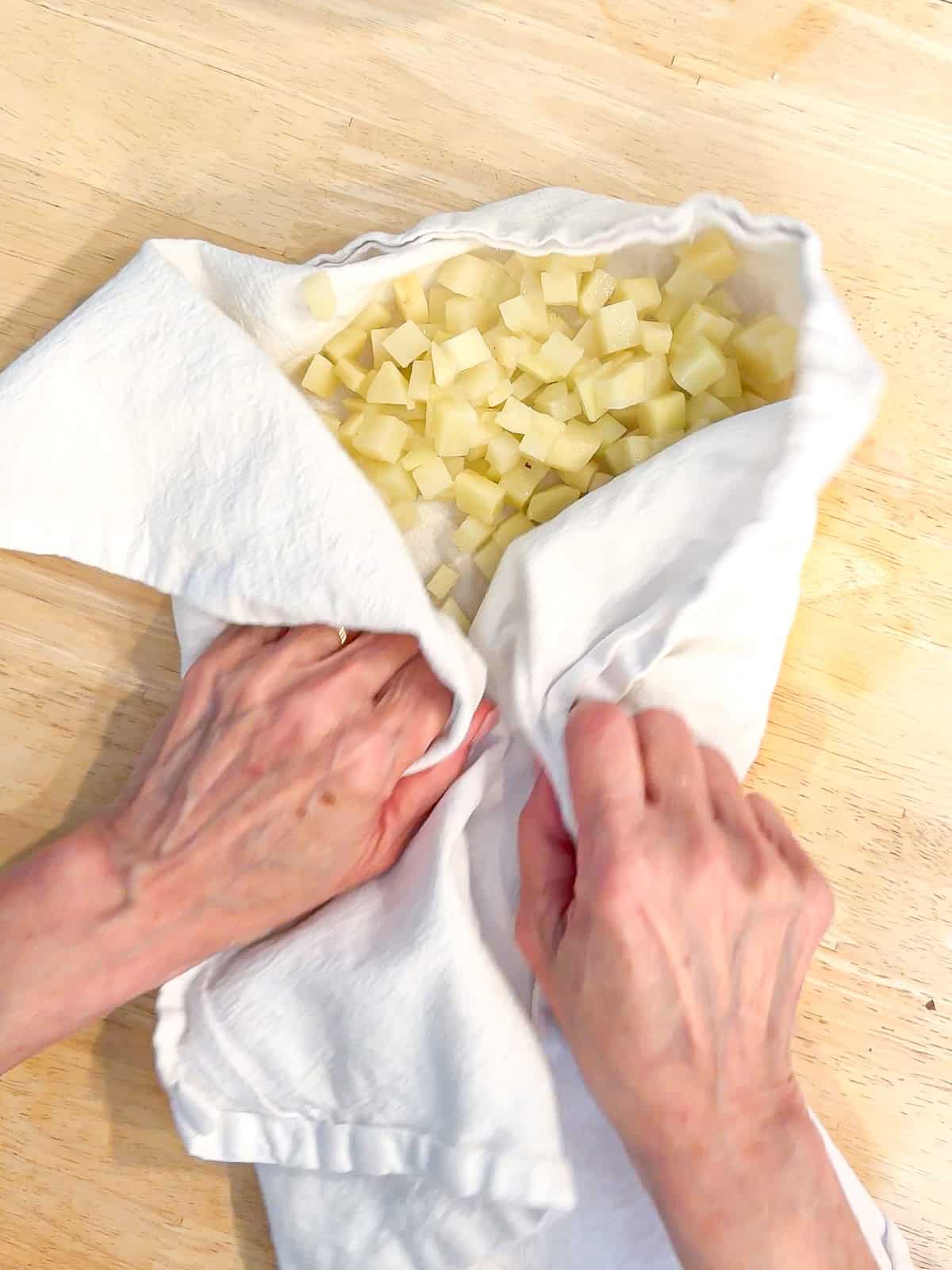 Drying microwave cooked diced potatoes in a white kitchen towel.