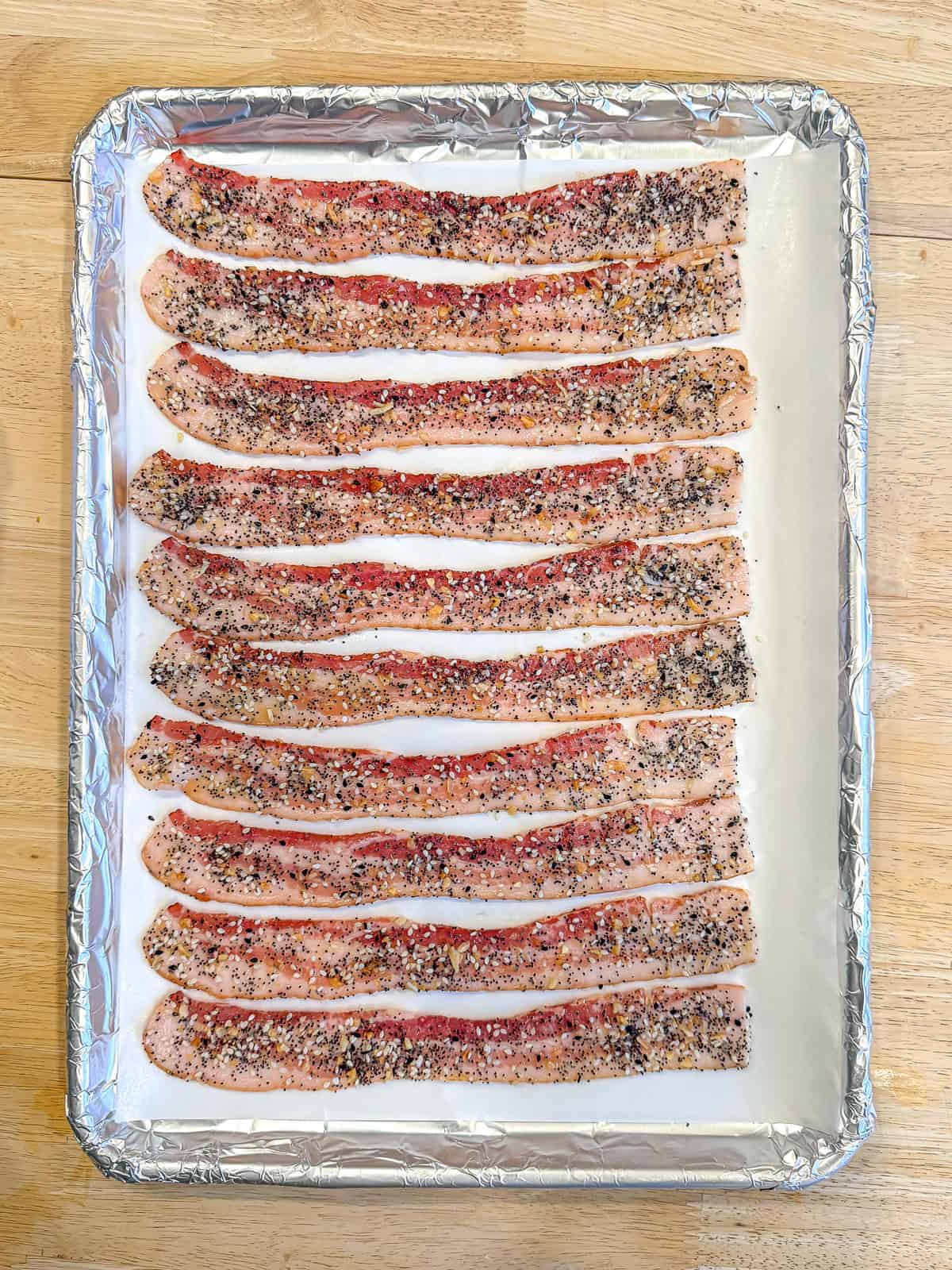 Unbaked everything seasoned bacon on a parchment paper and foil lined pan.