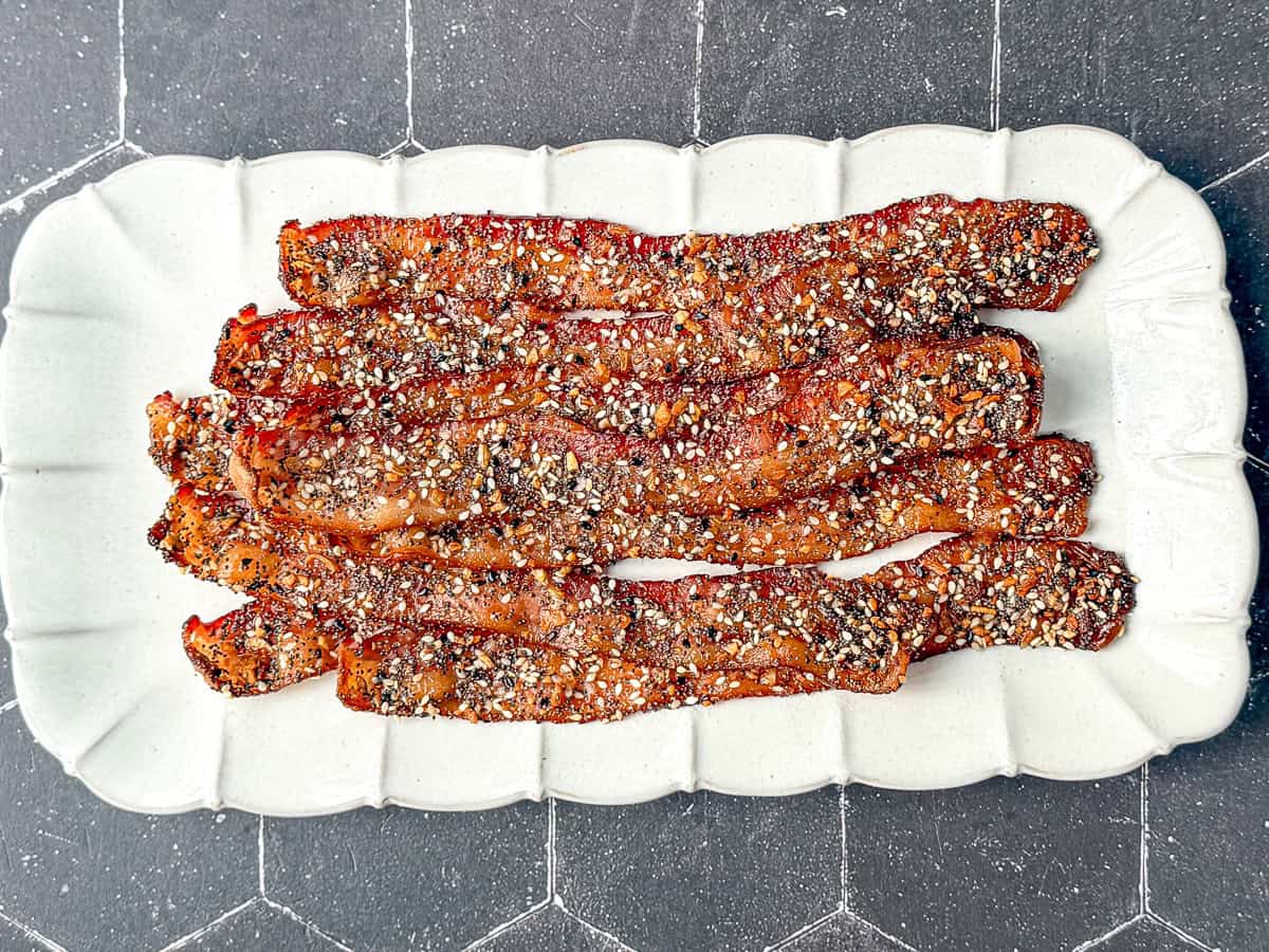 Everything seasoning candied bacon on a white plate.