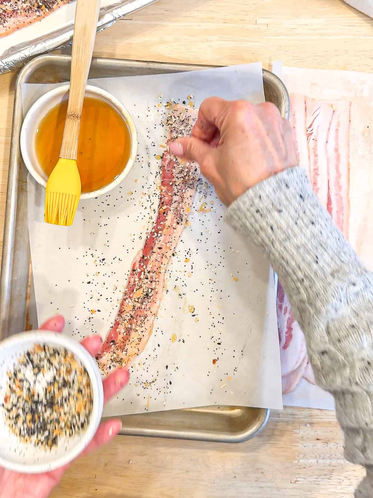 Sprinkling everything seasoning on a strip of bacon.