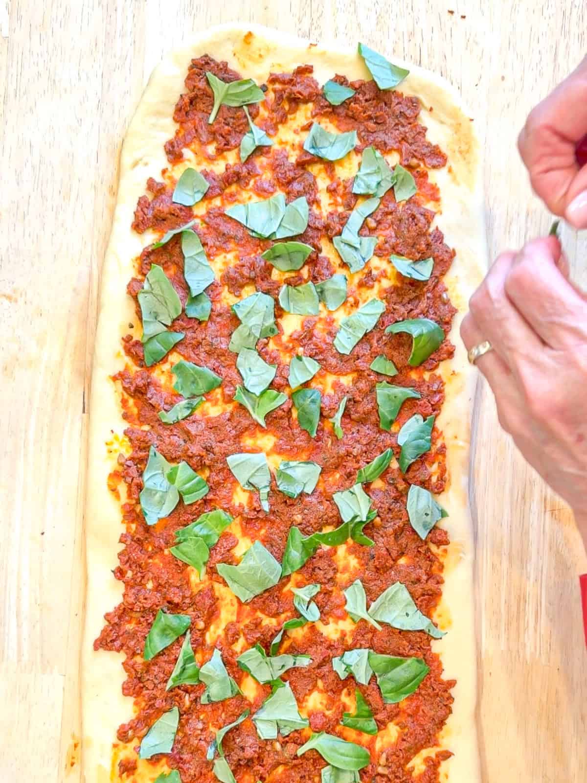 Hand tearing basil leaves over bread dough.