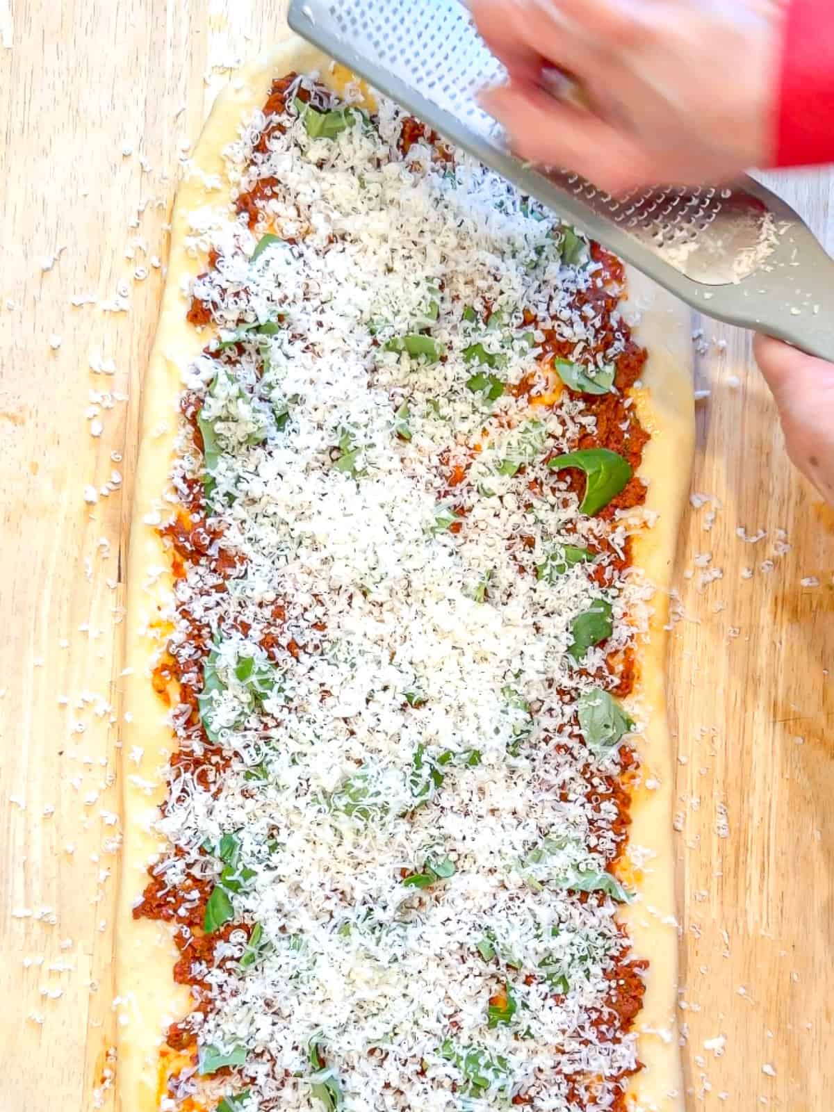 Grating Parmesan cheese over bread dough.