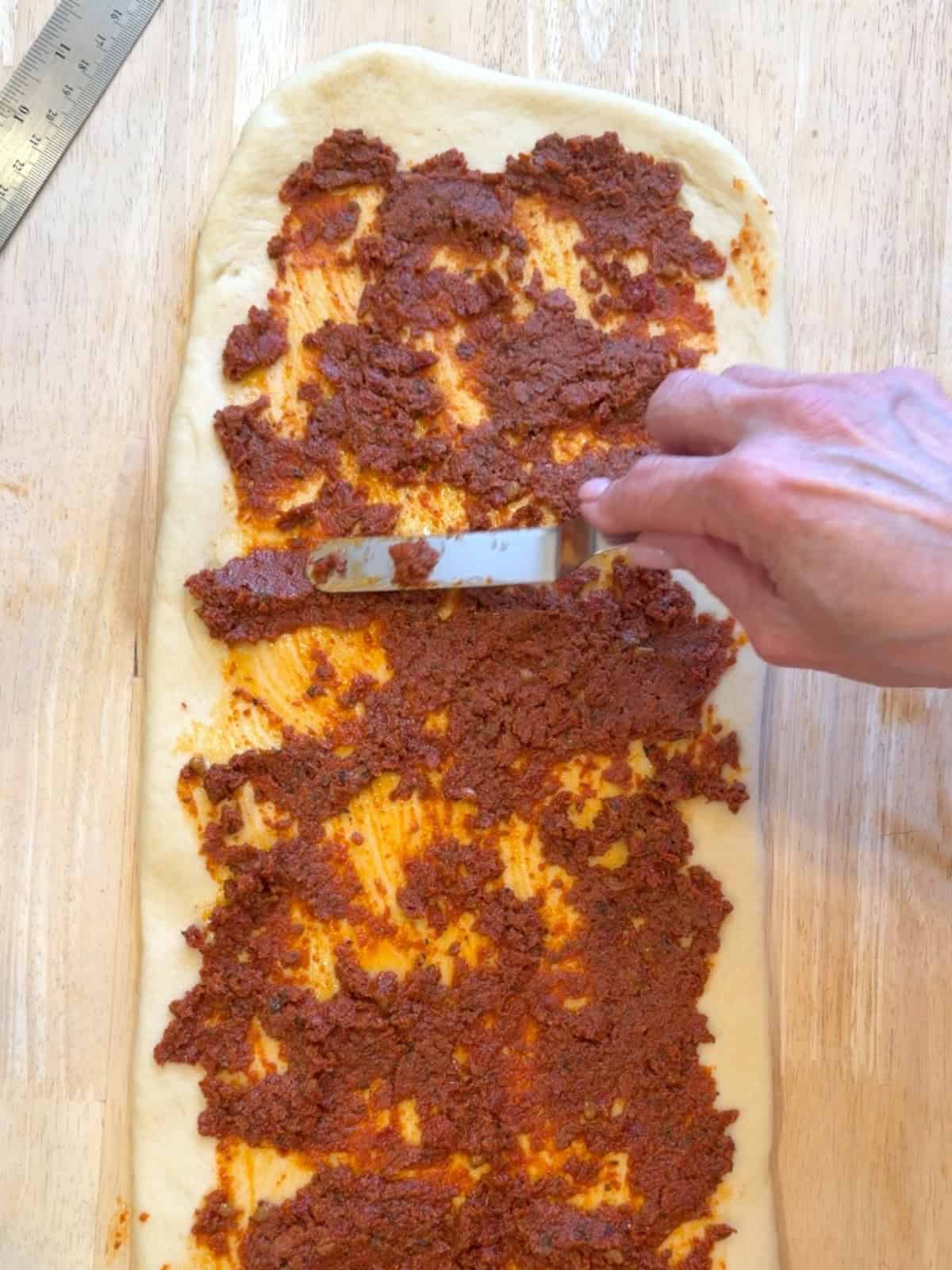 Spread spreading sun-dried tomato pesto over unbaked bread dough.