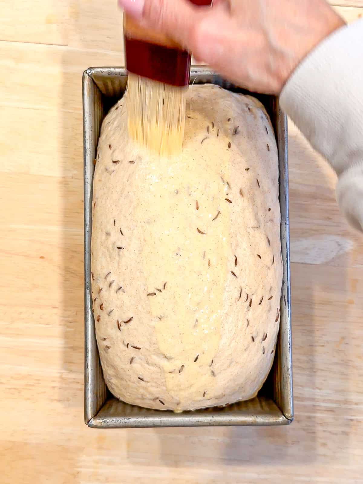 Brushing the egg wash on a loaf of rye bread before baking.