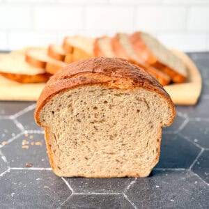 A loaf of rye bread on a black counter with a sliced loaf behind it.