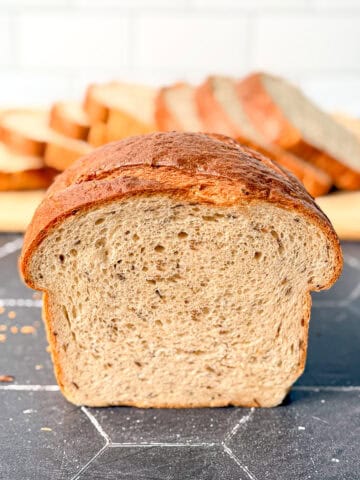 A loaf of rye bread on a black counter with a sliced loaf behind it.