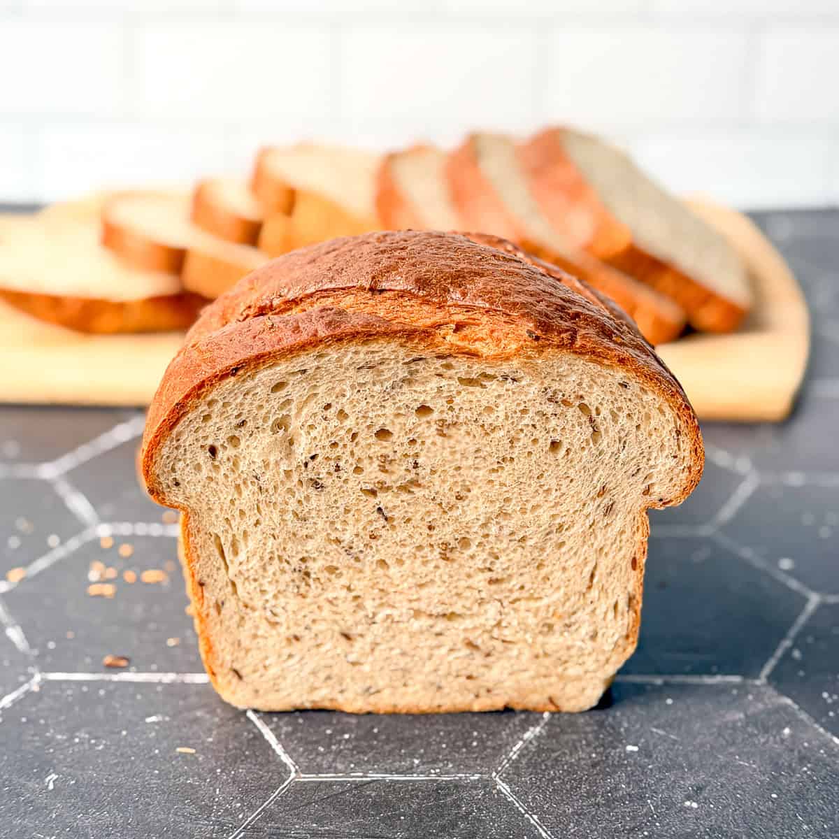 A loaf of rye bread on a black counter with a sliced loaf behind it.