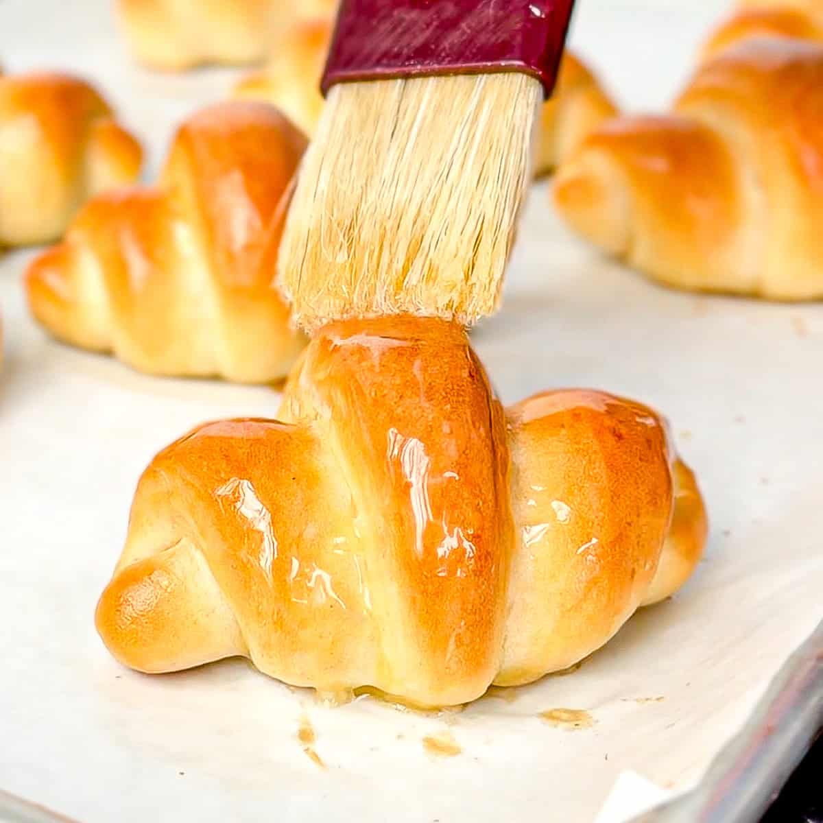 Brushing melted butter on a fully baked crescent roll.