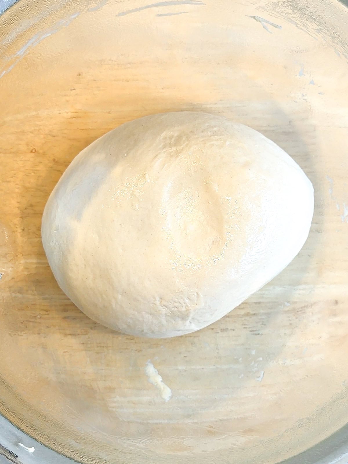 Fully kneaded dough in a glass bowl.