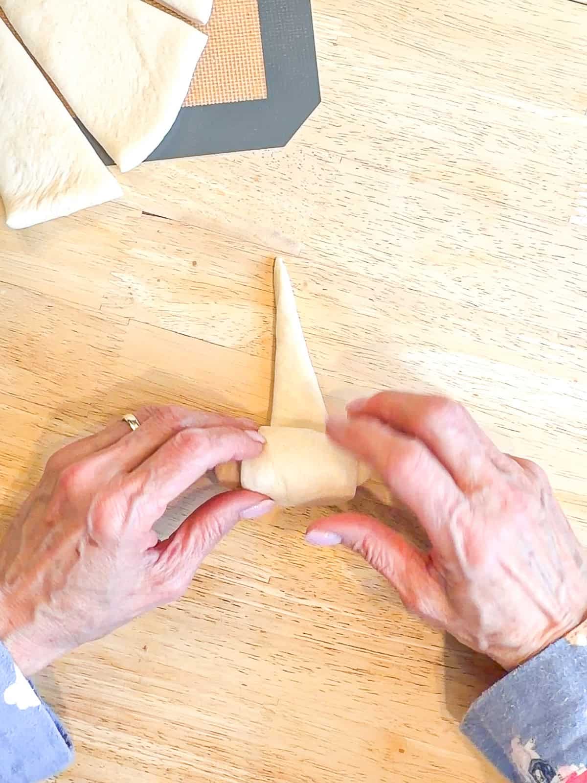 Rolling a triangle of dough into a crescent roll.