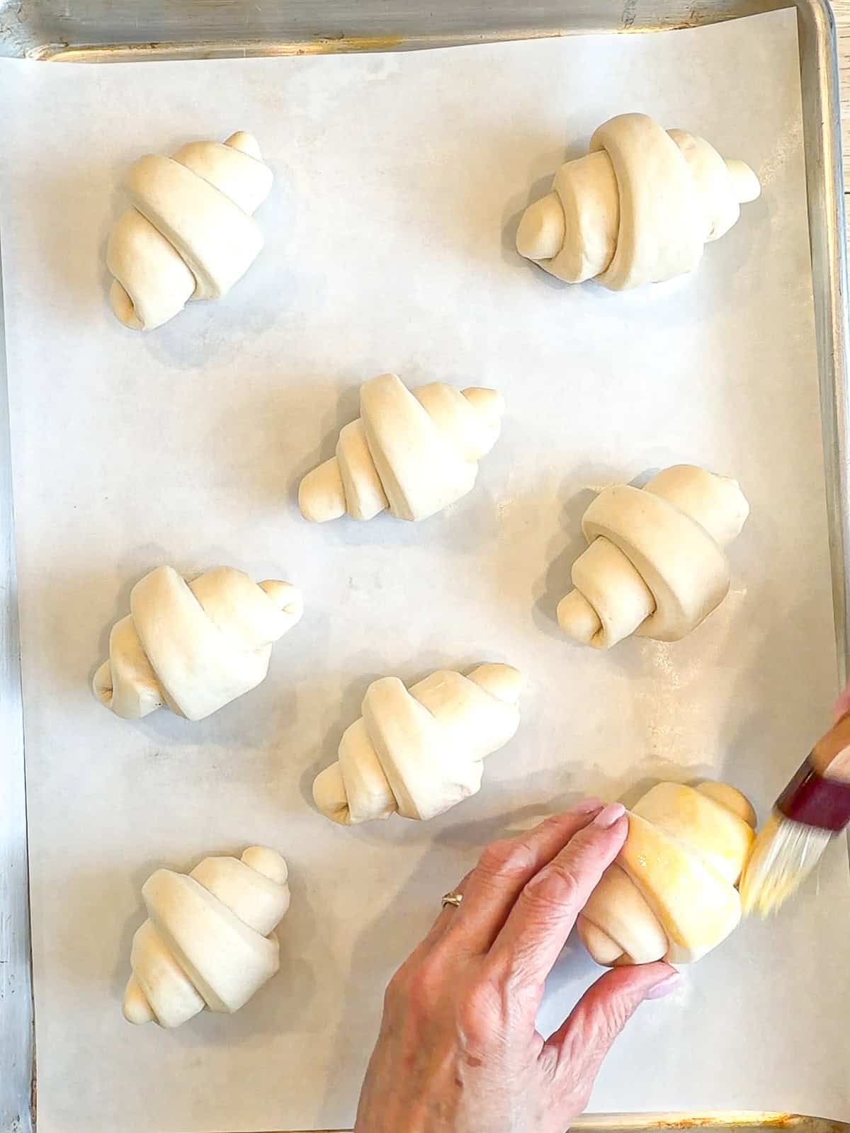Brushing egg wash on unbaked crescent rolls.