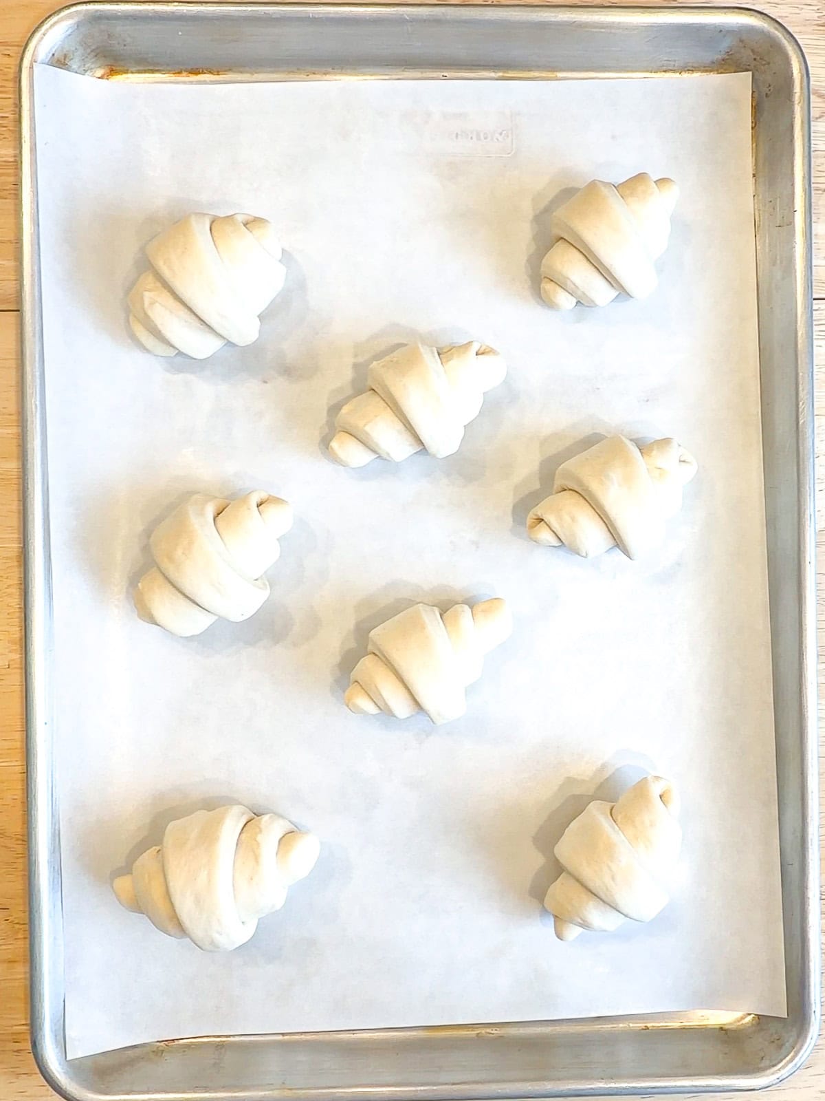 Unbaked crescent rolls on a parchment paper lined sheet pan.