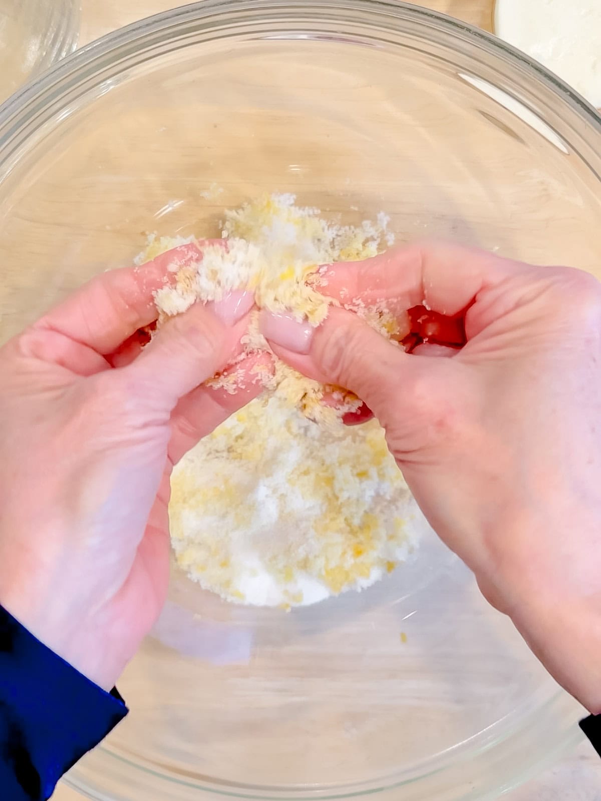 Rubbing lemon zest into sugar in a glass bowl.