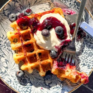 Lemon ricotta waffle with blueberries and with ricotta on a blue floral plate.