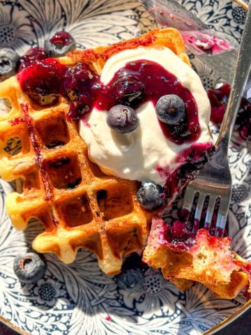 Lemon ricotta waffle with blueberries and with ricotta on a blue floral plate.