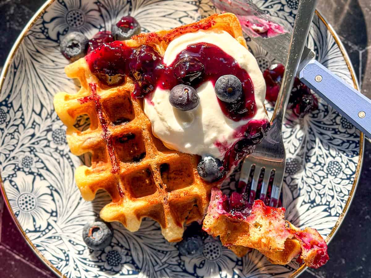 Lemon ricotta waffle with blueberries and with ricotta on a blue floral plate.