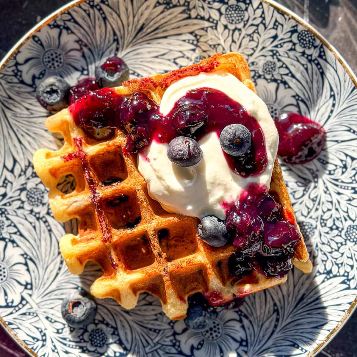 Lemon ricotta waffle with blueberries and with ricotta on a blue floral plate.