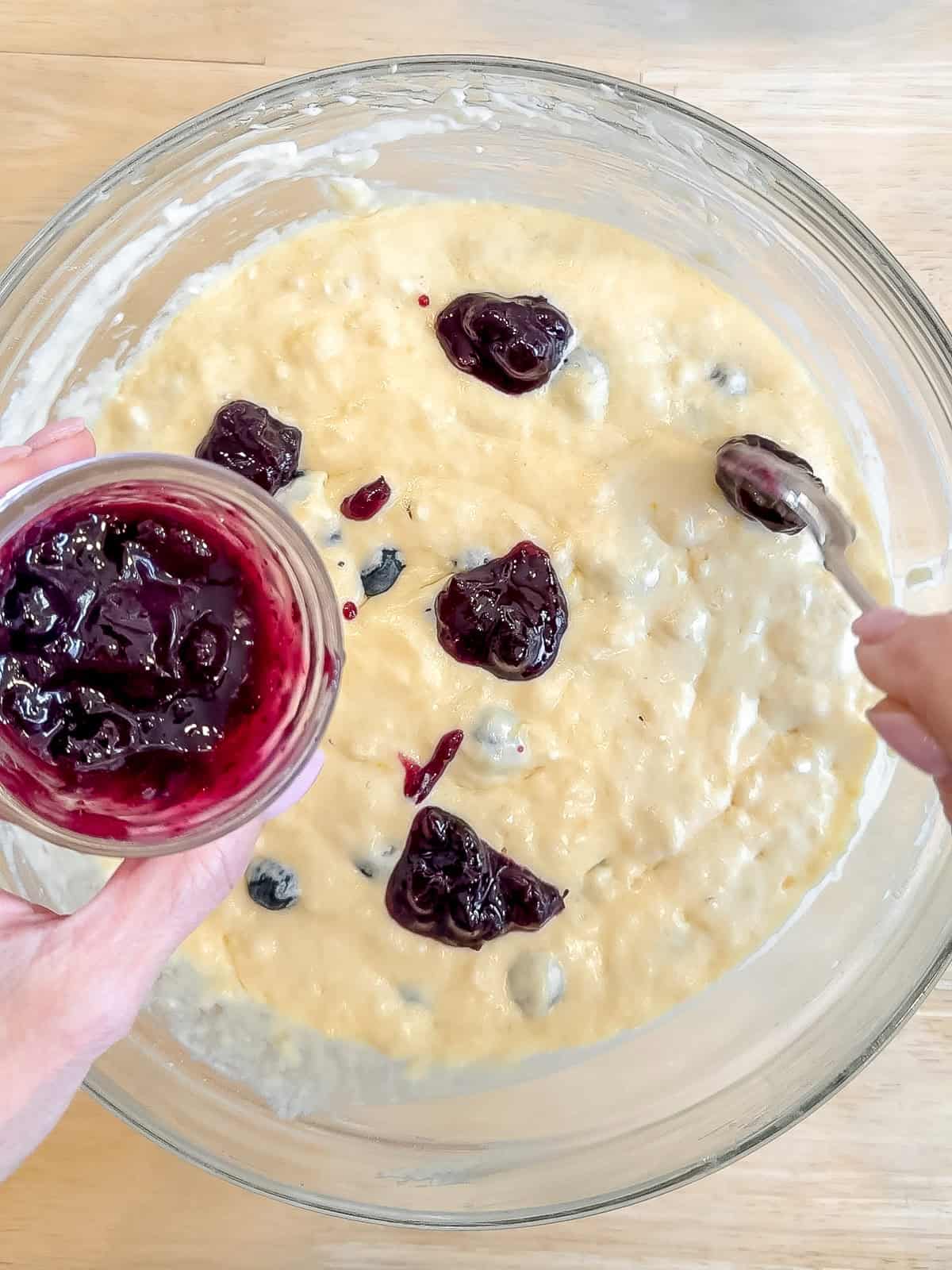 Placing spoons of blueberry jam on top of waffle batter.
