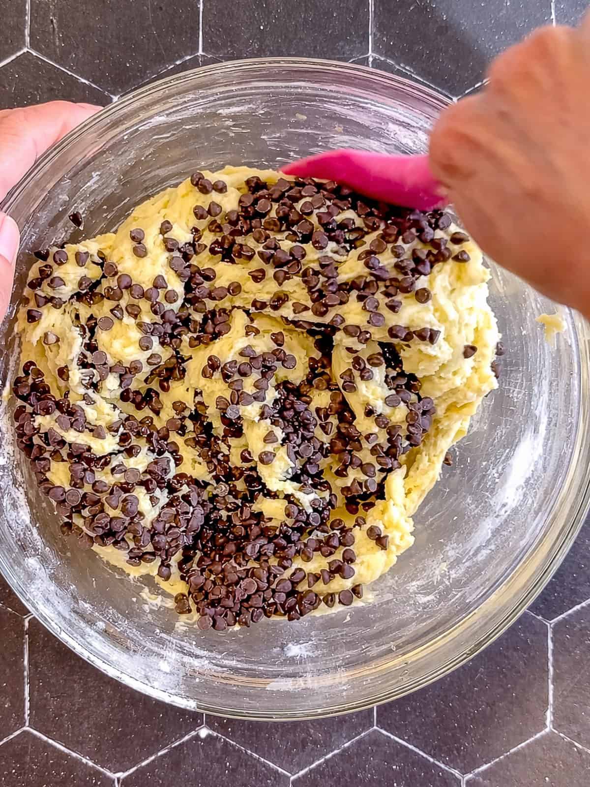 Folding chocolate chips into banana bread and a glass bowl.