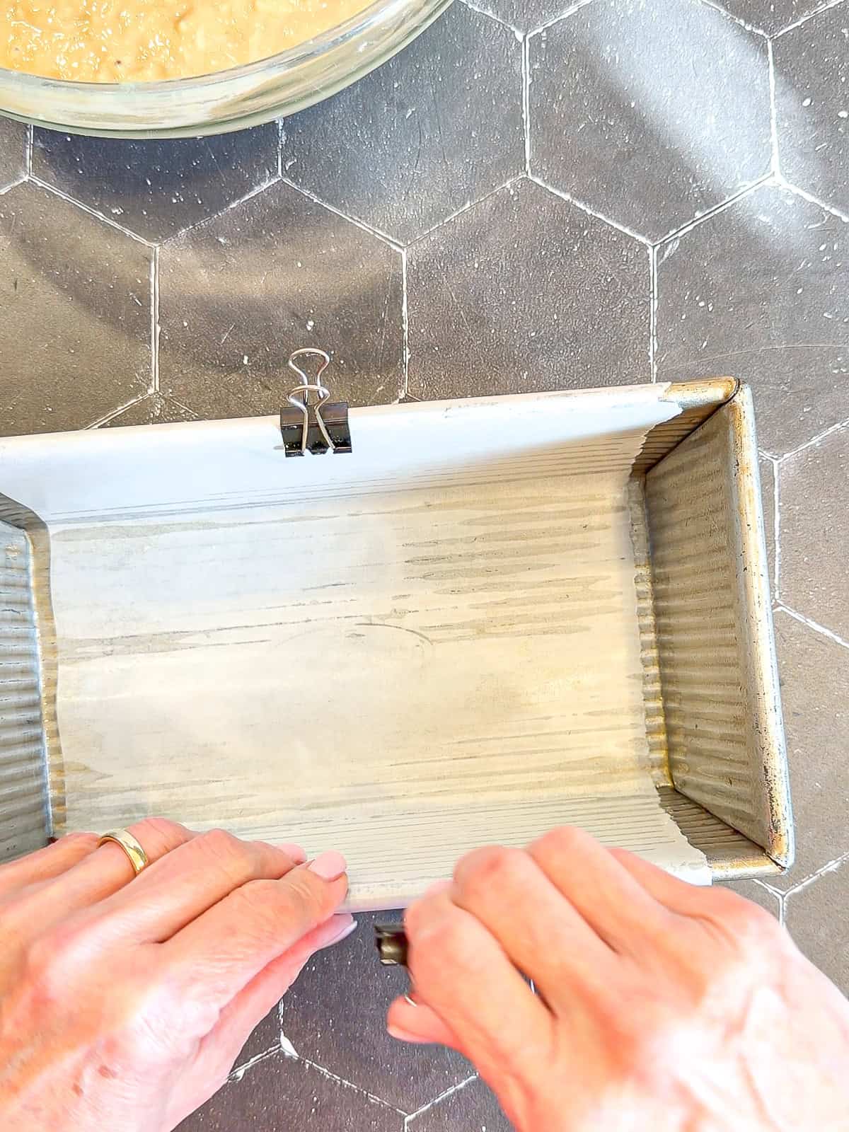 Clipping a piece of parchment paper into a loaf pan.