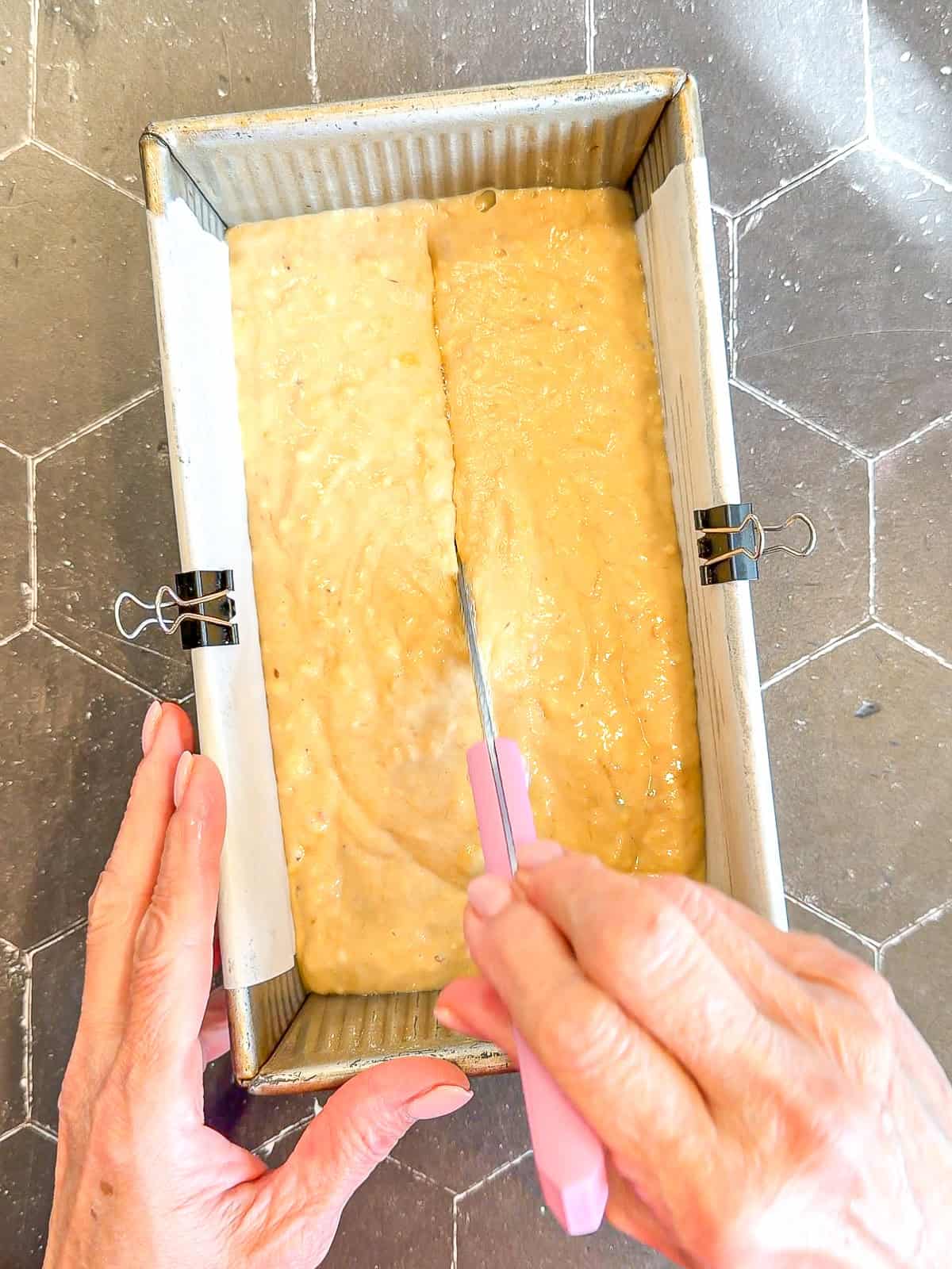 Using a knife too make a line in the center of banana bread batter in a loaf pan.