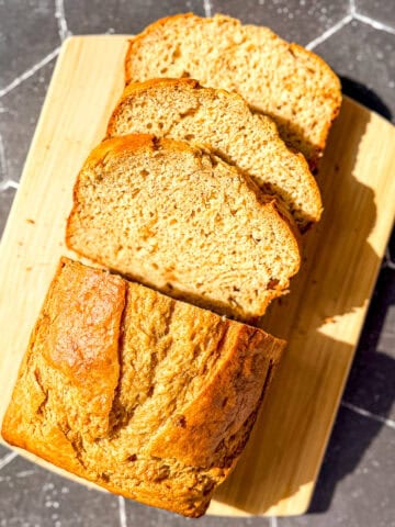 Sliced banana bread on a wooden cutting board on a black backdrop.