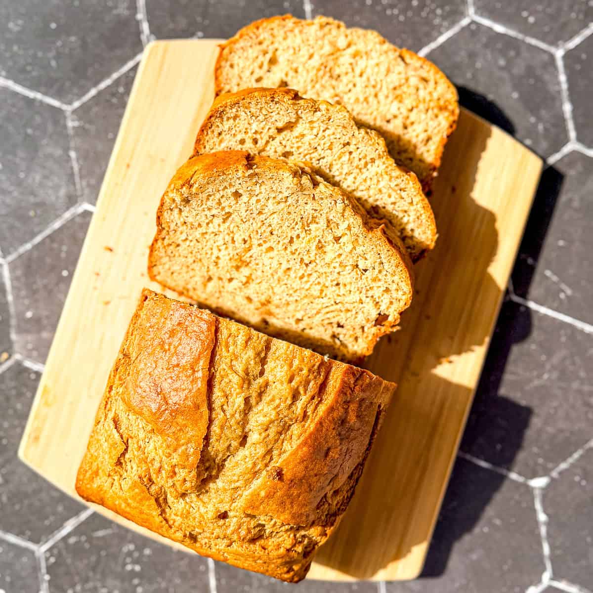 Sliced banana bread on a wooden cutting board on a black backdrop.