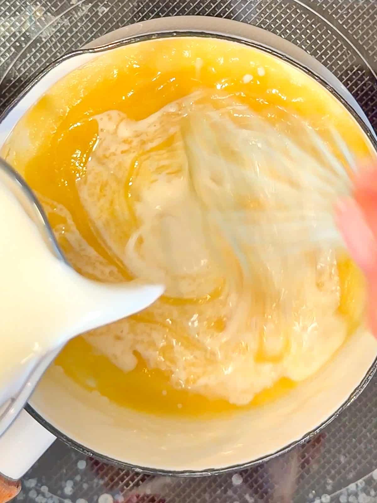 Adding a milk to flour and butter in a sauce pan to make a bechamel sauce.