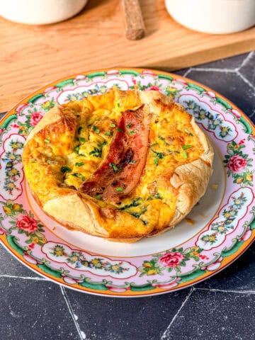 Spinach and bacon soufflé on a pink floral plate with two more soufflés in the background on a wooden cutting board