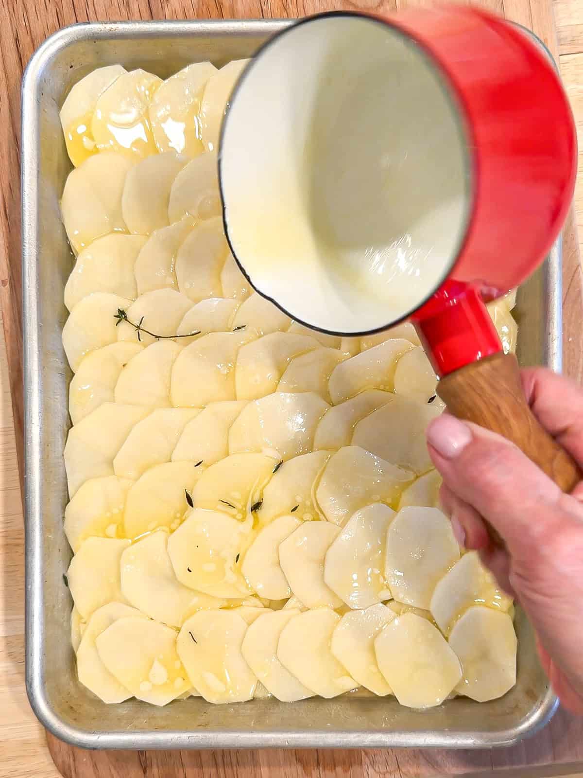 Drizzling melted butter over a layer of potatoes in a sheet pan.
