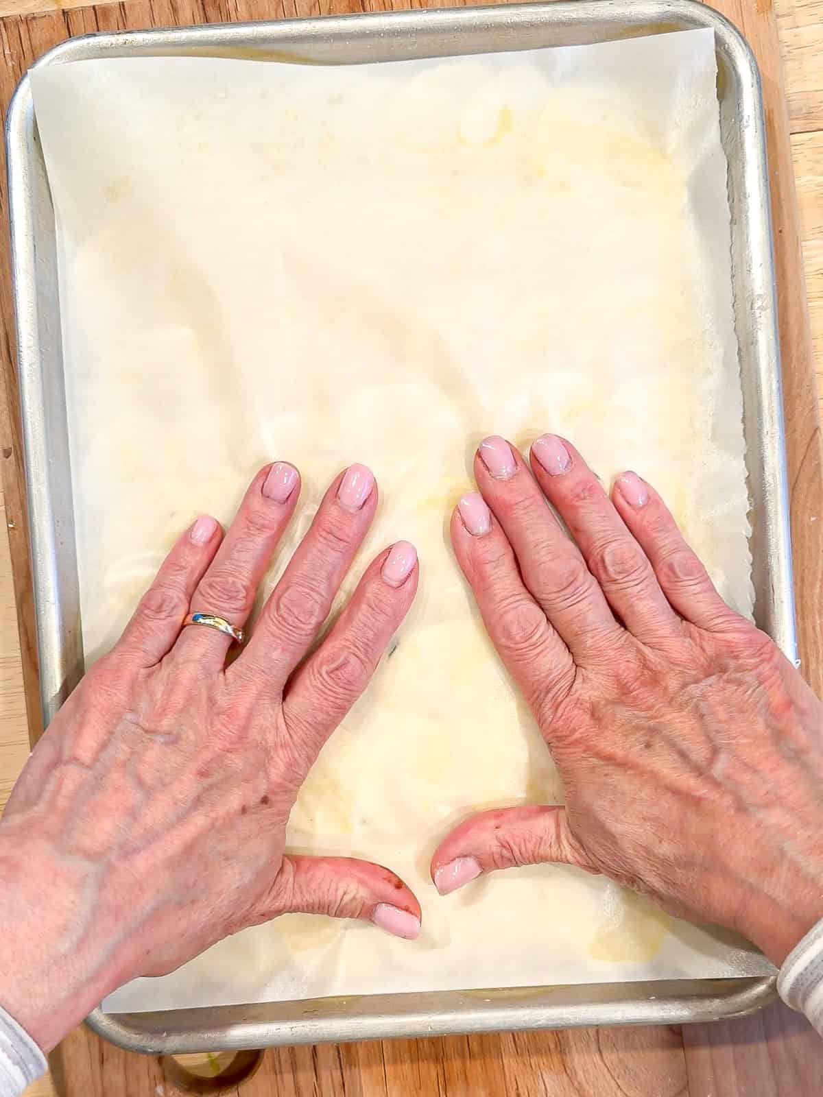 Pressing a piece of parchment paper on top of potatoes in a sheet pan.
