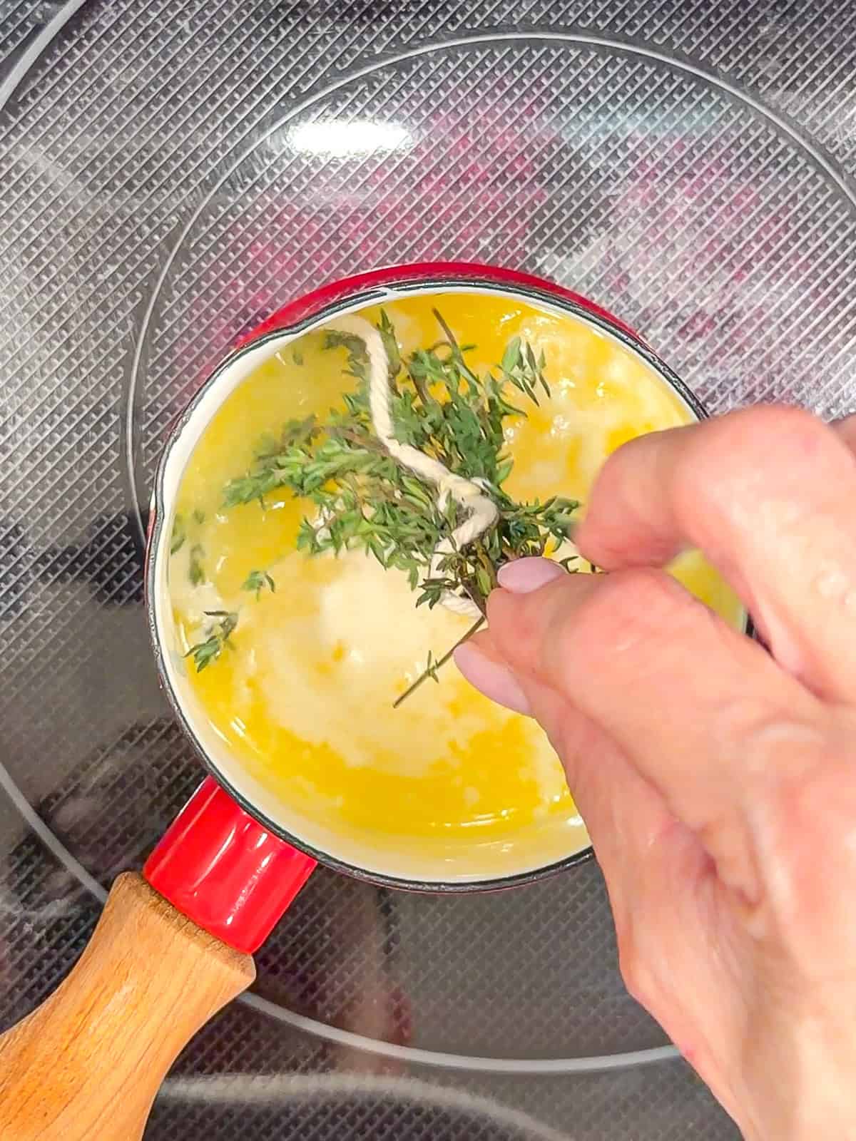 Adding thyme sprigs to melted butter in a small sauce pan.