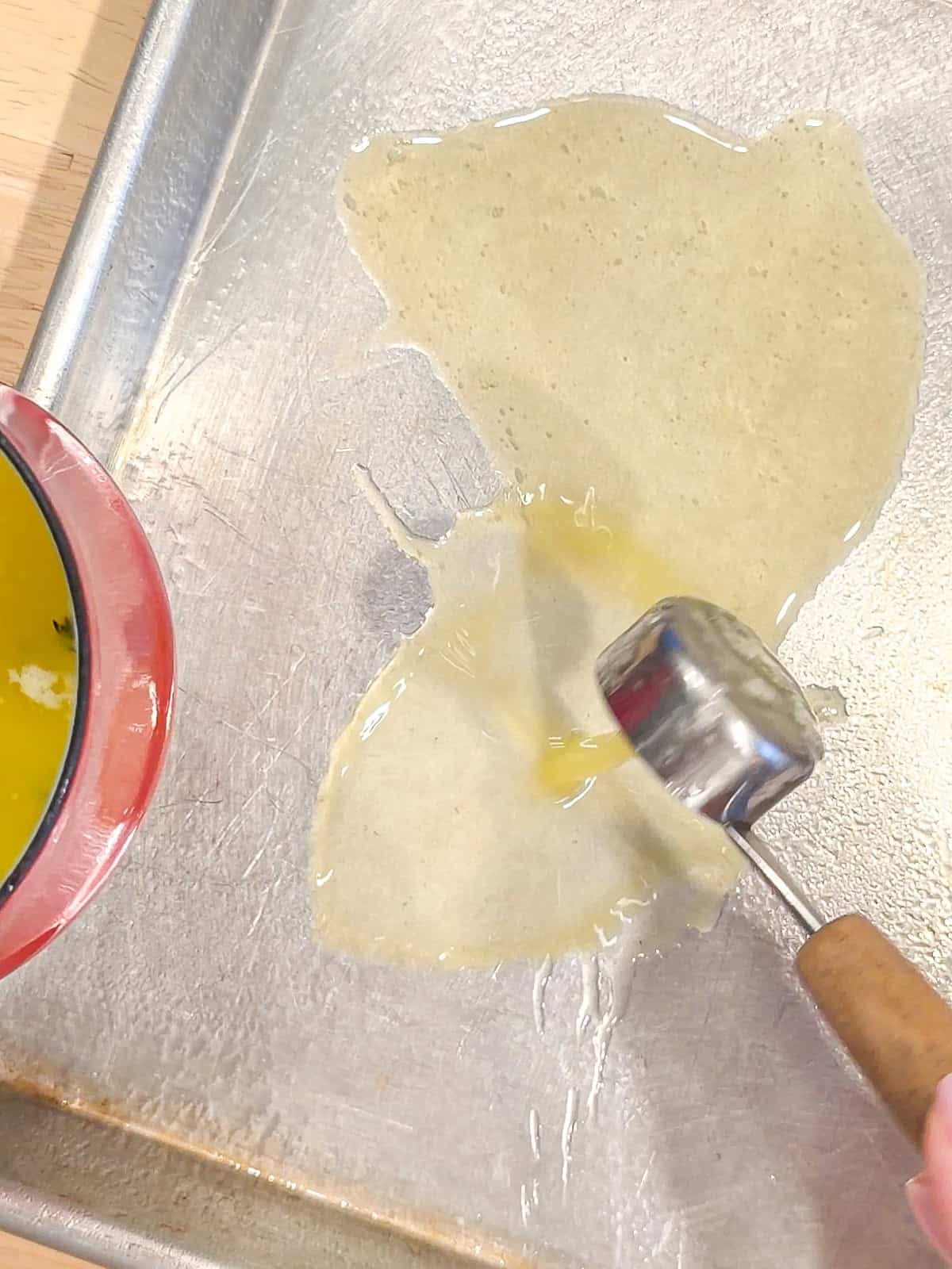 Placing a tablespoon of melted butter into a sheet pan.