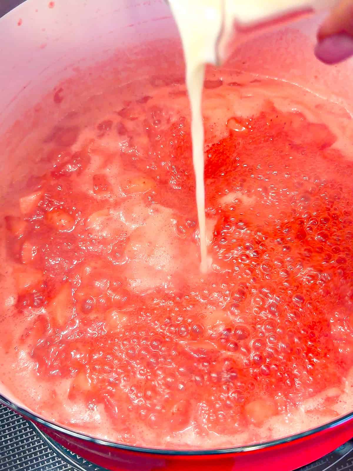 Adding lemon juice and cornstarch slurry to simmering strawberry jam.