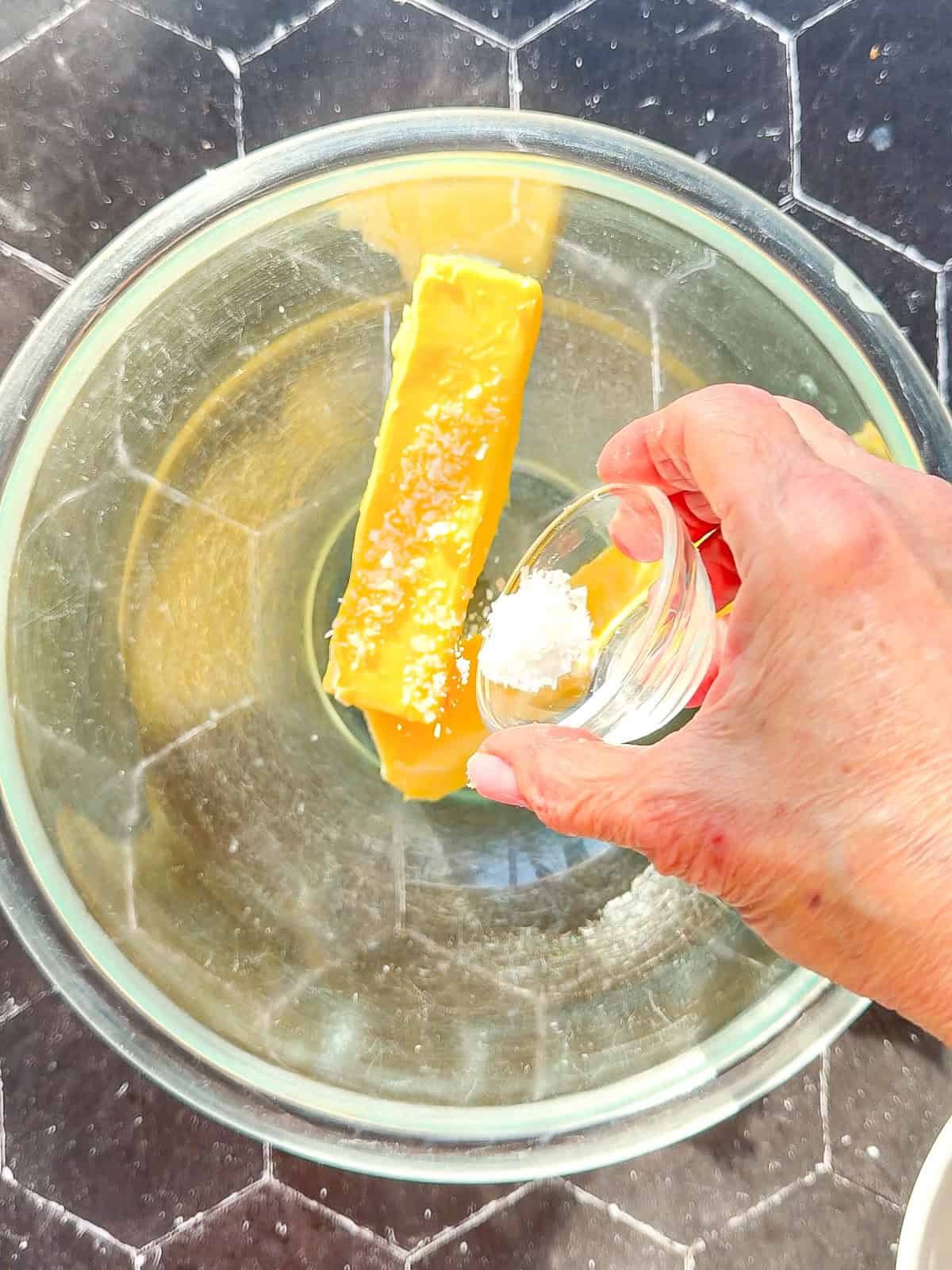 Adding salt to two sticks of butter in a glass bowl.