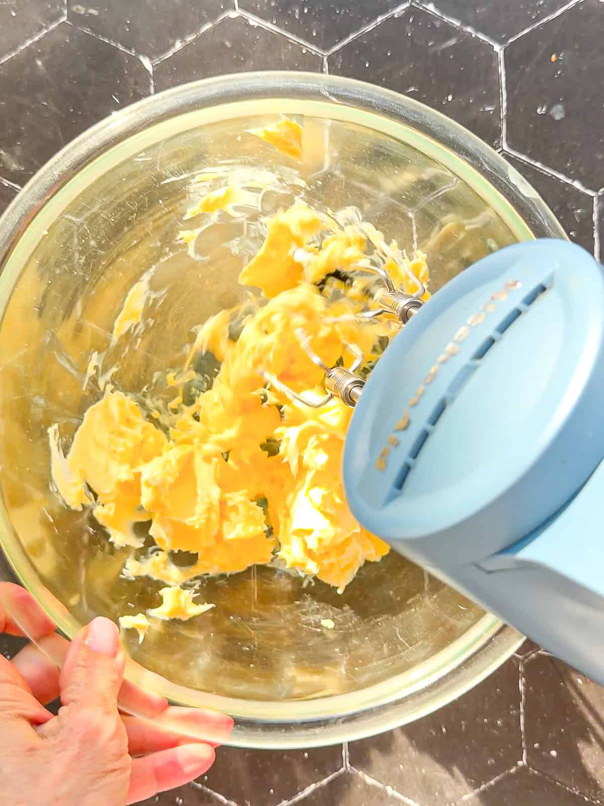 Using a hand mixer to whip butter in a glass bowl.