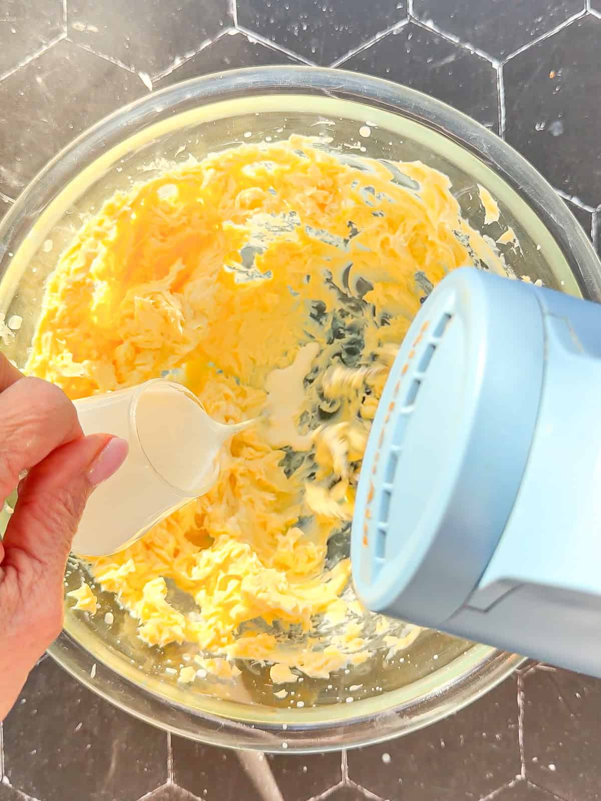 Drizzling cream into butter when beating with a hand mixer in a glass bowl.