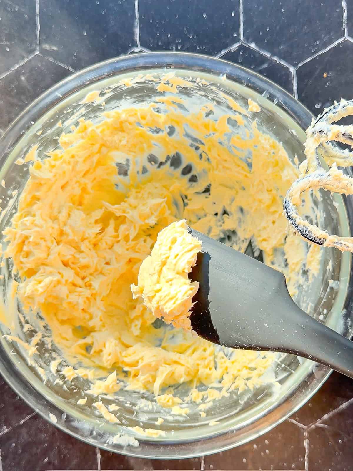Spatula holding whipped salted butter above a glass bowl of butter.
