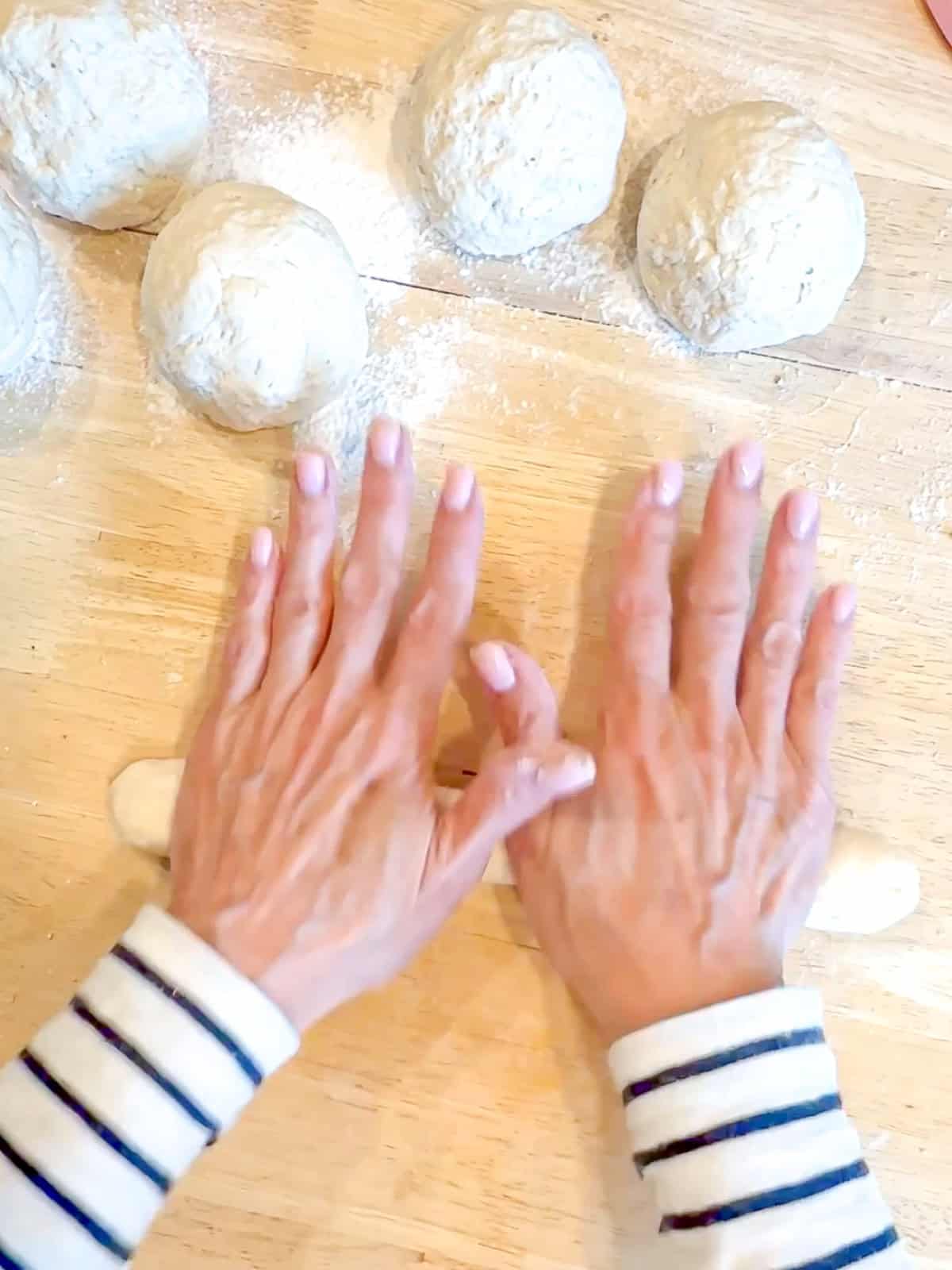 Using the palms of my hands to shape a bowl of dough into a long rope.