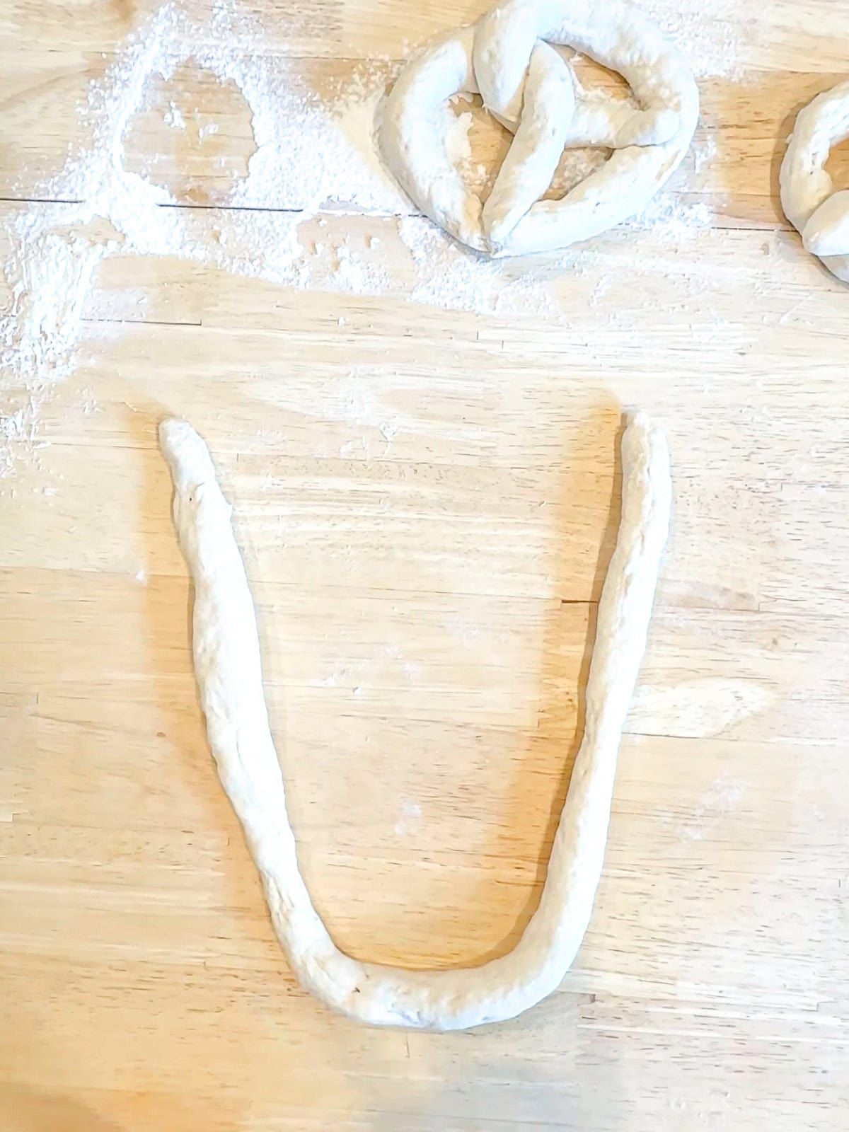 Shaking rope of pretzel dough into a U shape.