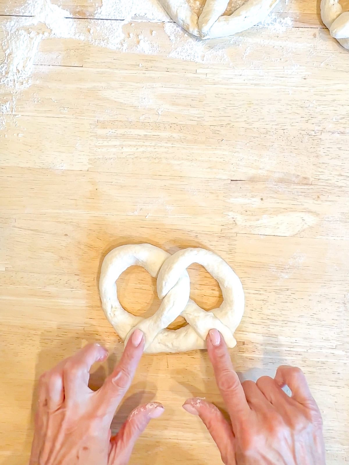 Bringing dough strands down to form classic pretzel shape.