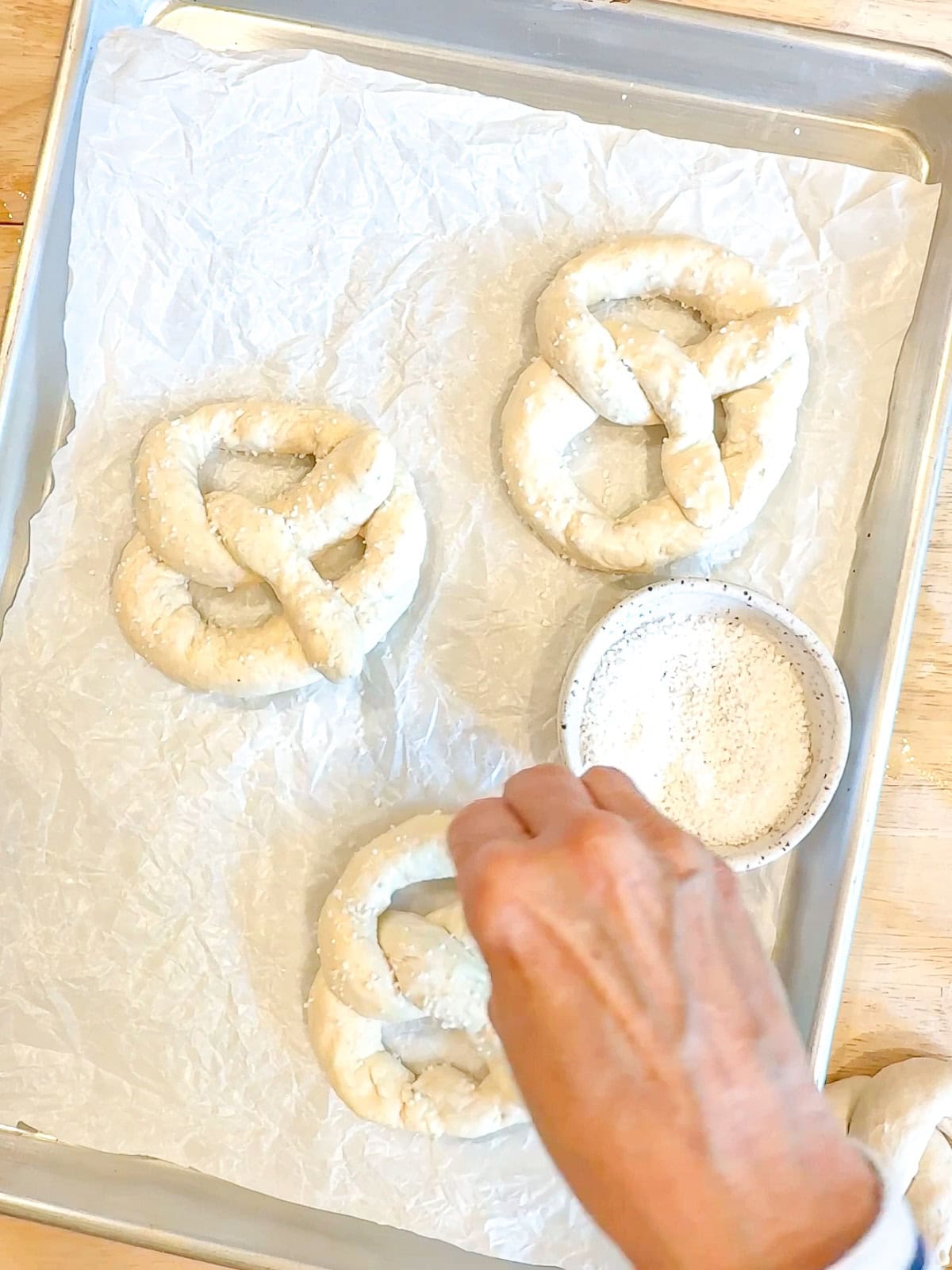 Sprinkling pretzel salt on un baked pretzels.