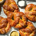 Soft pretzels on parchment paper with mustard and pretzel salt.