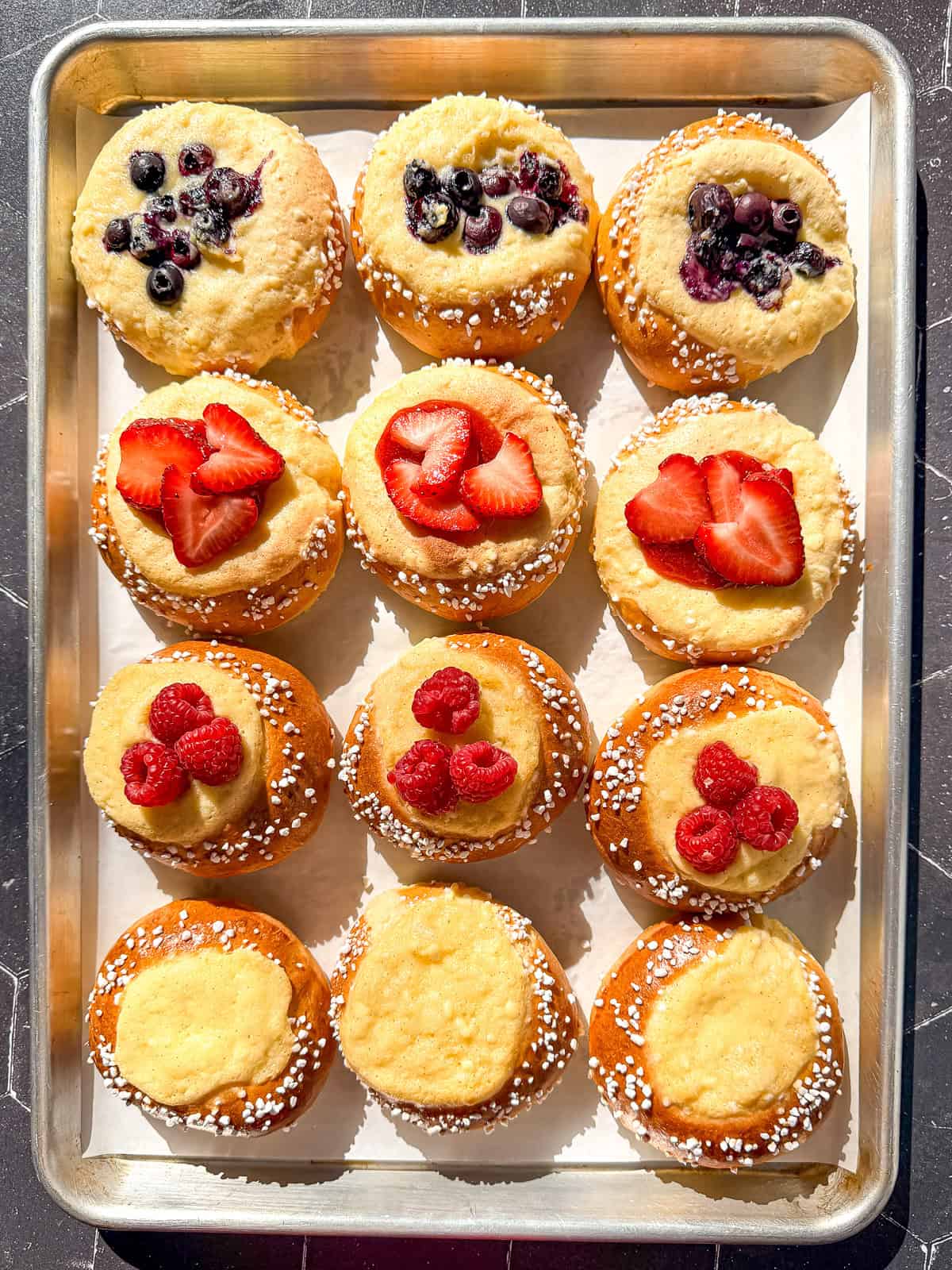 Berry topped brioche danishes on a pachment paper lined sheet pan.
