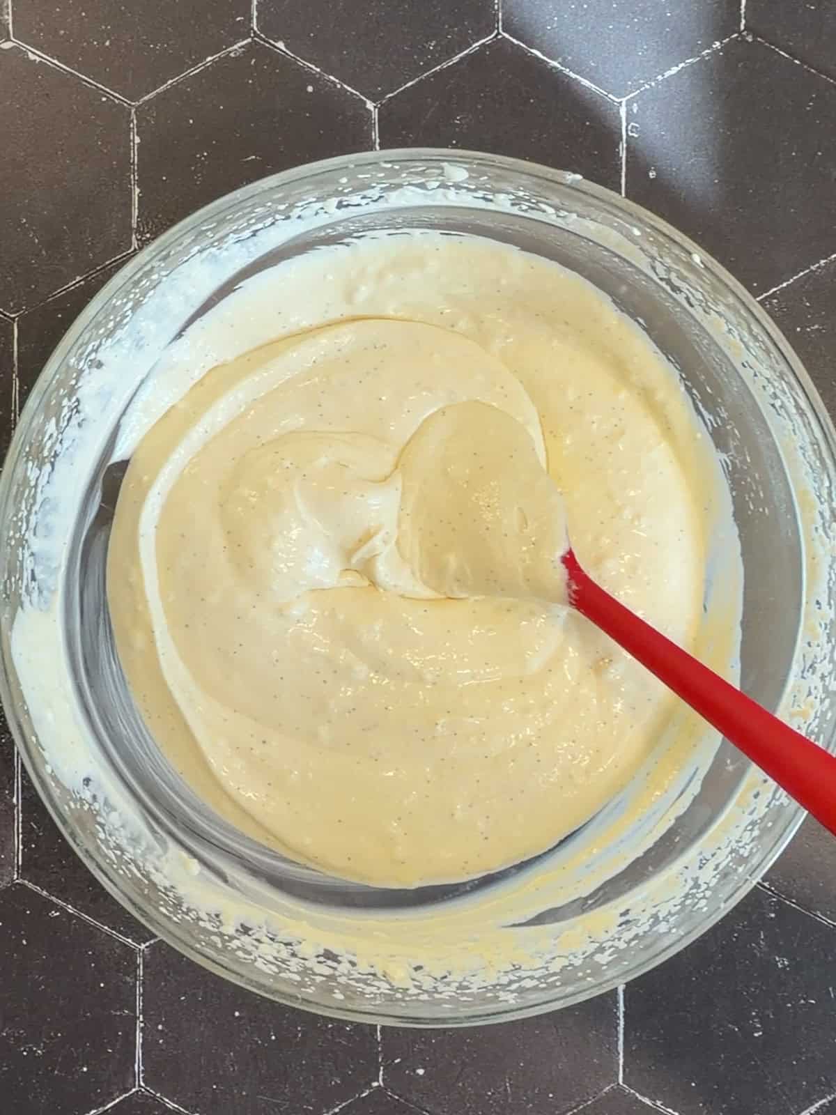 Creamy mixture in a white bowl with a red spatula.