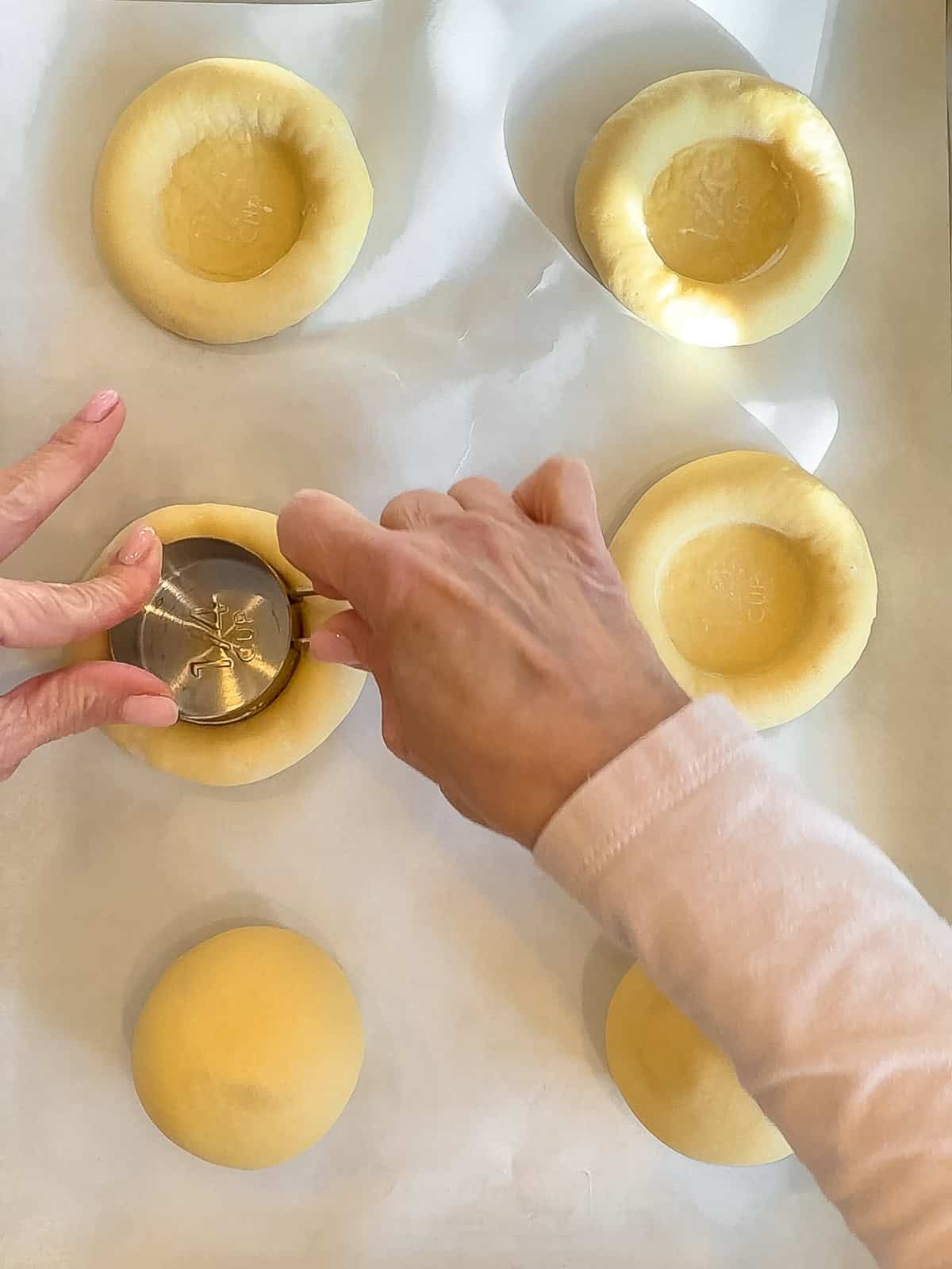 Using a measuring cup to create a depression in a dough ball.