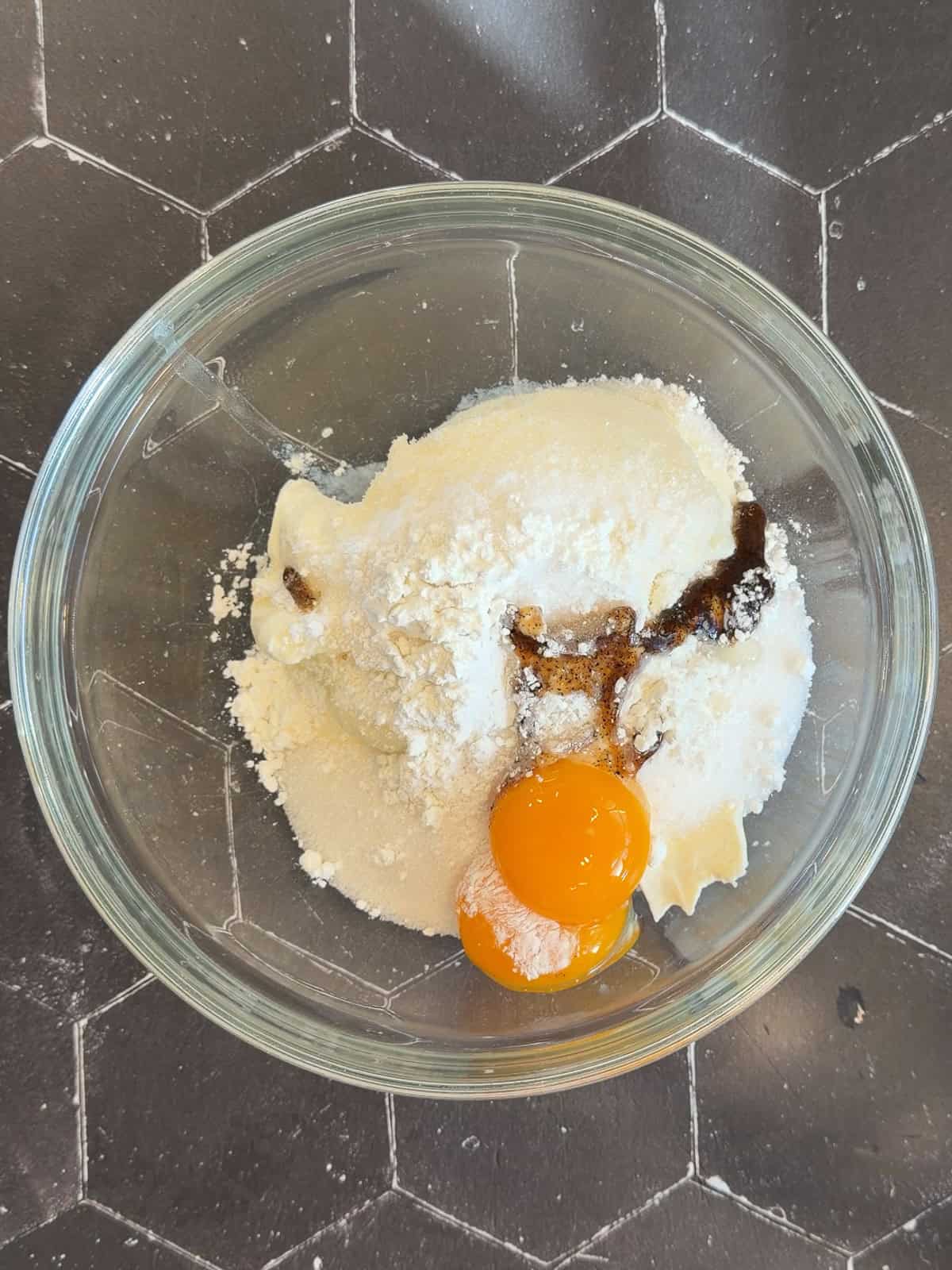 White ingredients with two egg yolks and vanilla in a glass bowl.