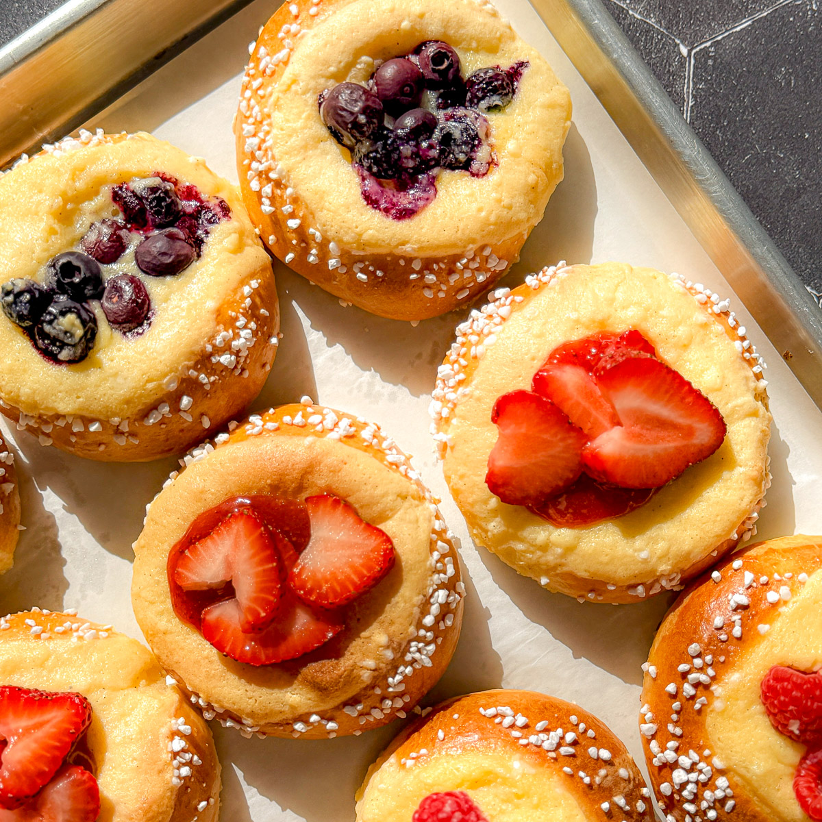 Berry topped brioche danishes on a parchment paper lined sheet pan.